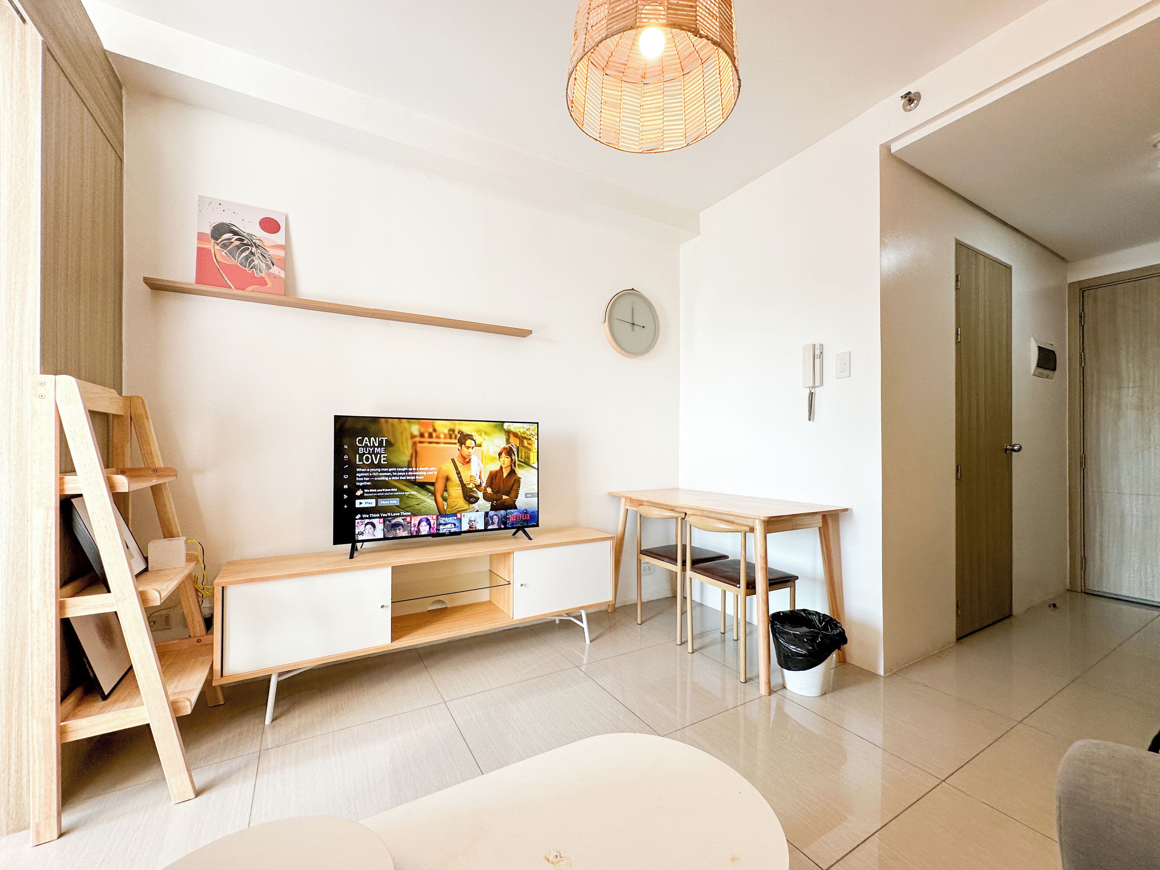 A modern living room with a flat-screen TV, wooden furniture, a small table, and a wicker ceiling light.