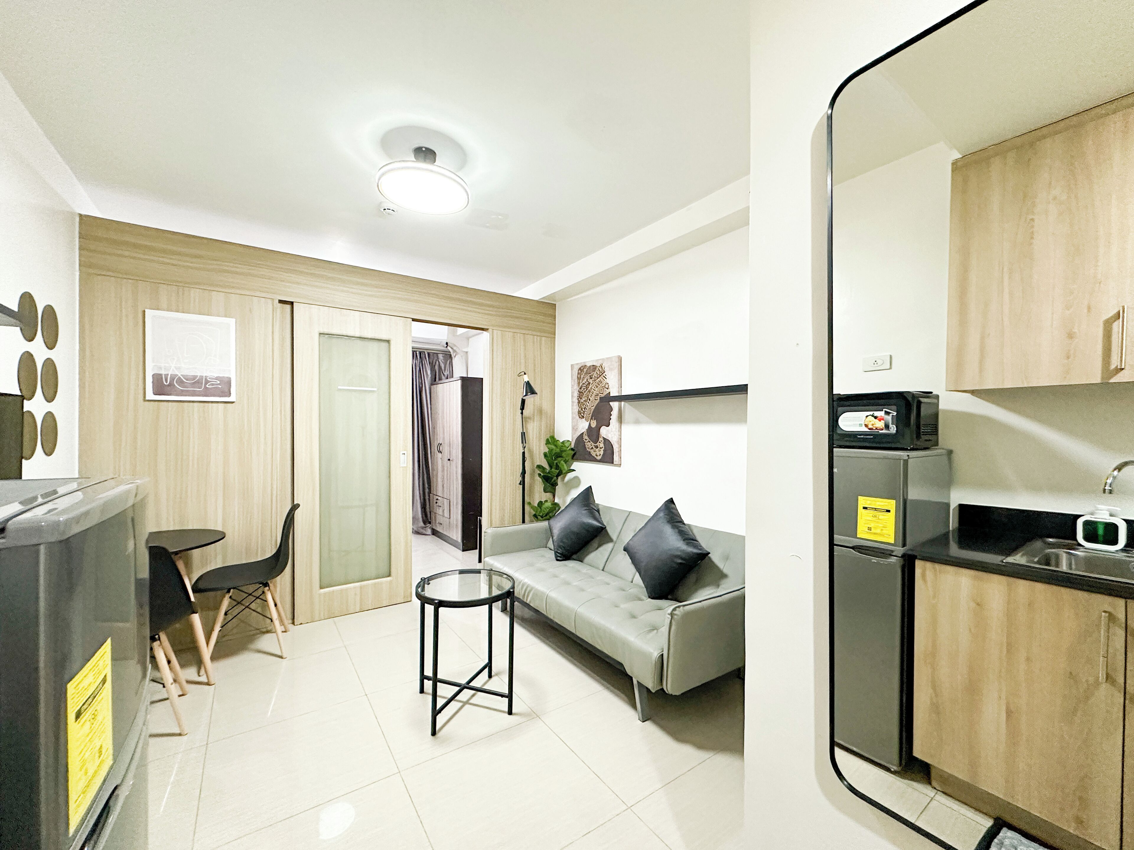 A compact living space with a kitchenette, a sofa, a small round table, and a cabinet.