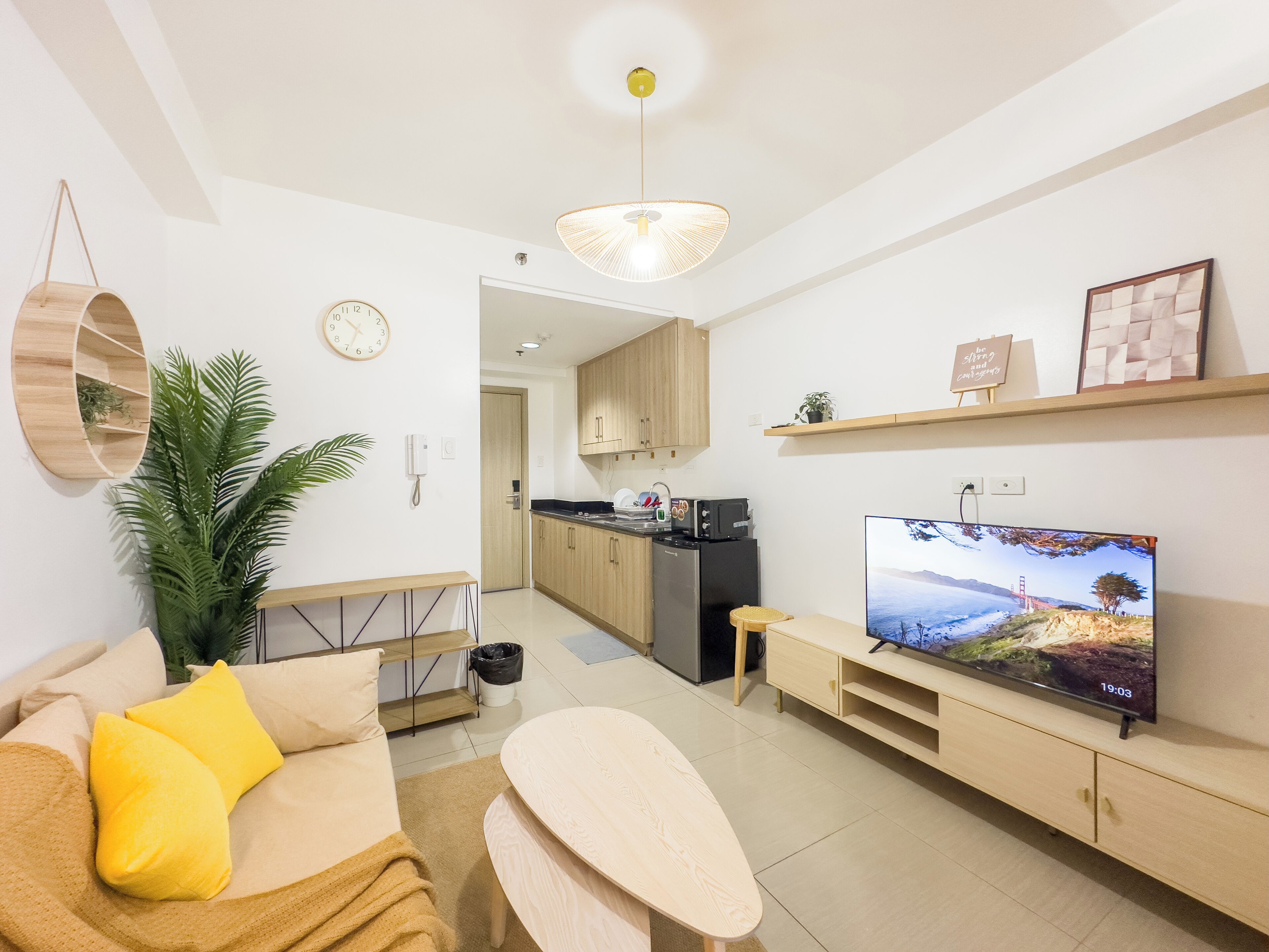 Una sala moderna con un sofá, una mesa de centro, un televisor y una cocina al fondo.