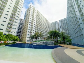 Un complejo residencial moderno con edificios de gran altura, una piscina central y zonas ajardinadas con palmeras.