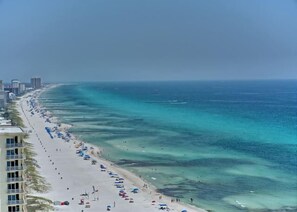 A beach with a long stretch of sand, clear blue water, and a row of buildings along the shore. - Breathtaking Views in this 2BR 2BA Condo w/Beach Chairs @ The Gulf Crest! (Panama City Beach)