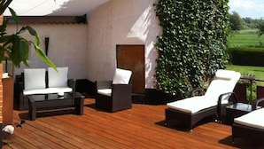 Una terraza de madera con muebles de exterior, incluyendo un sofá, sillas y una tumbona.