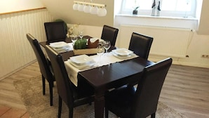 Comedor con una mesa de madera oscura dispuesta para cuatro personas, rodeada de sillas negras. Hay un mantel blanco, un jarrón con flores y una lámpara decorativa sobre la mesa.