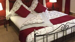 Una cama con dosel, almohadas rojas y una colcha estampada con motivos florales.