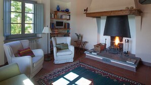 A cozy living room with a fireplace, a bookshelf, a comfortable chair, and a window with shutters. - Tuscan Holiday Home With Pool (Chiusi)