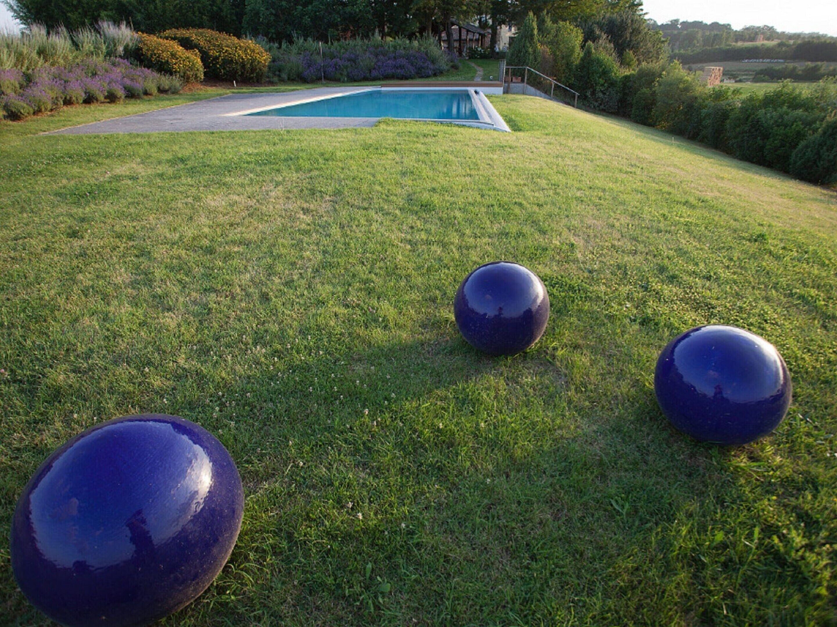 Uma área gramada com três objetos esféricos e uma piscina ao fundo.