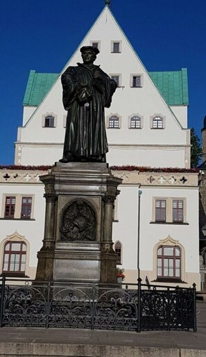 Eine Statue vor einem weißen Gebäude mit grünen Dächern und verzierten Fenstern.