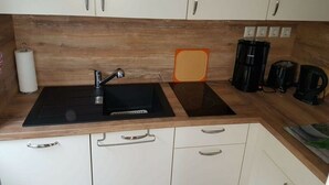 A kitchen with a black sink, white cabinets, and a wooden backsplash. - Haus Elfi Modern Retreat (Lutherstadt Eisleben)