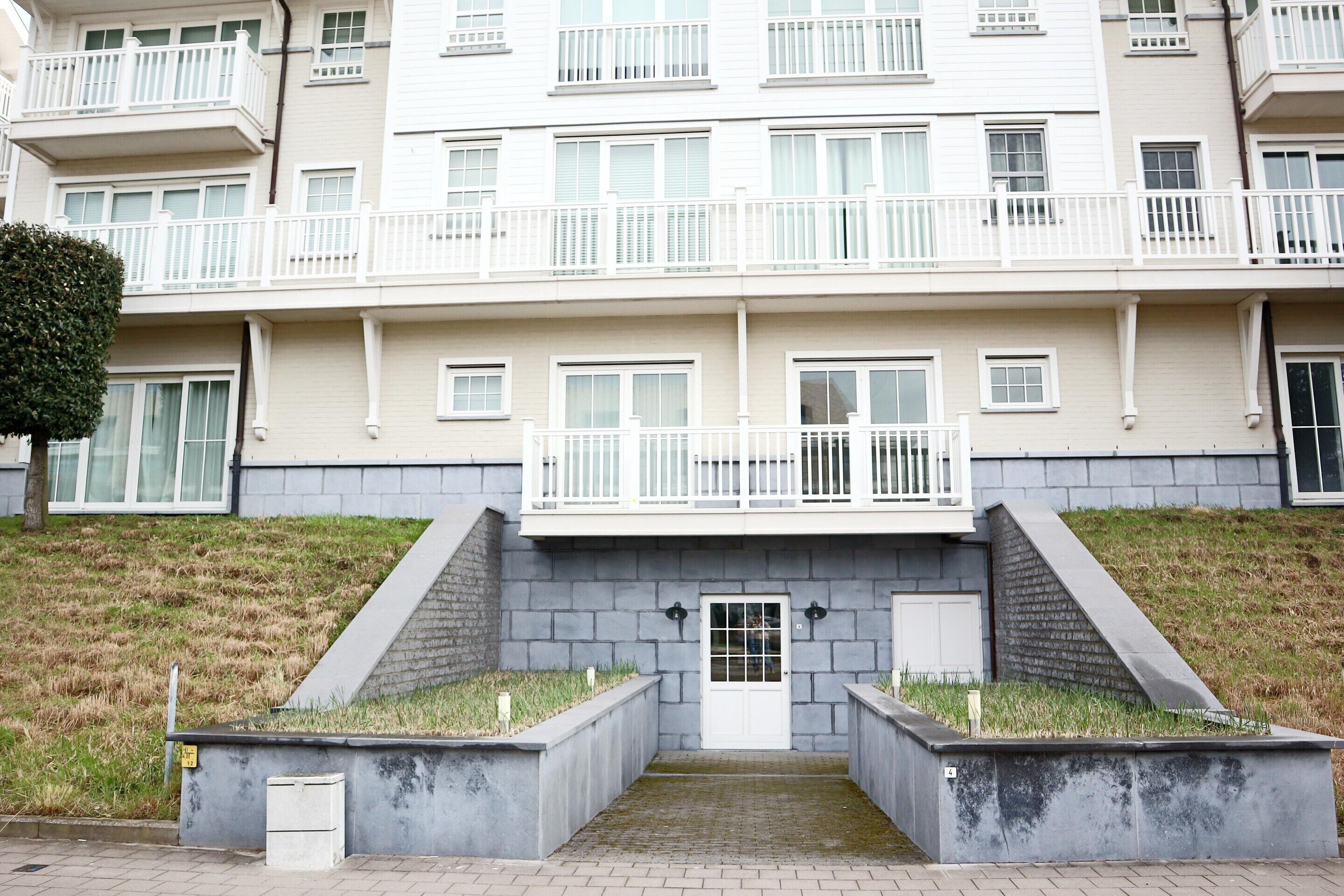 A multi-story residential building with balconies, a central entrance, and a small garden area.