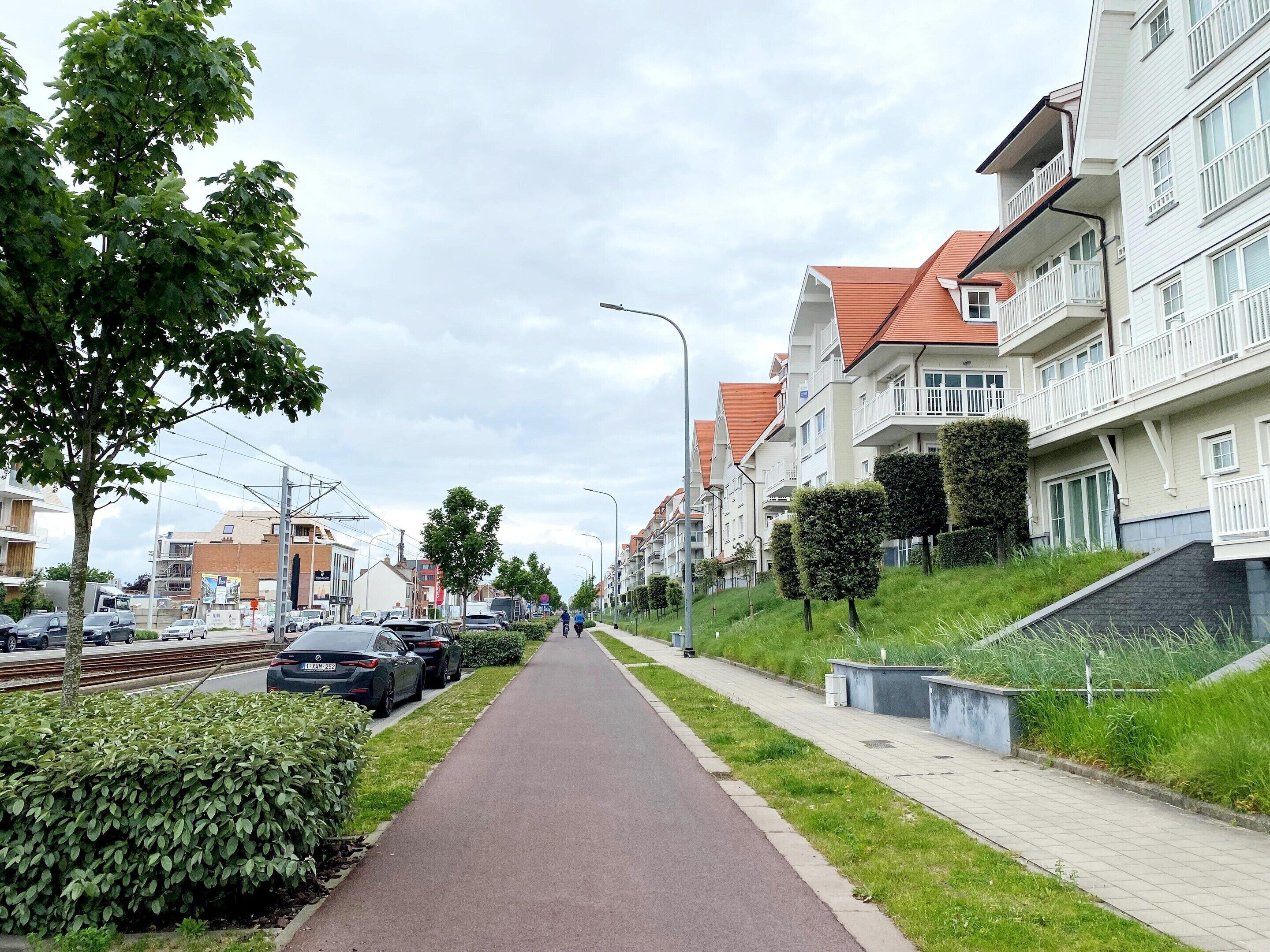 A residential street with modern apartment buildings, a bike path, and parked cars.