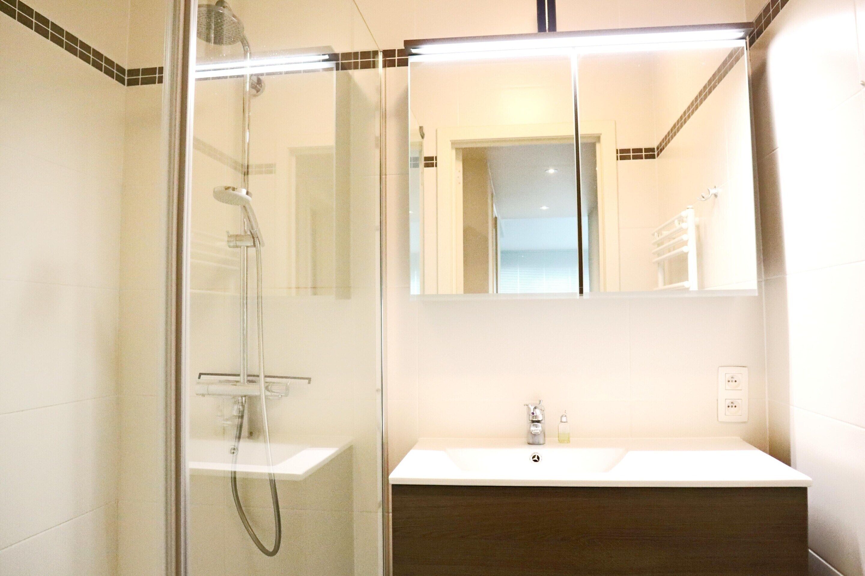 A modern bathroom with a glass-enclosed shower, a white sink, and a mirror above it.