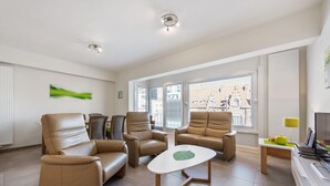 En moderne stue med lædersofaer, et sofabord og store vinduer med udsigt over byen.