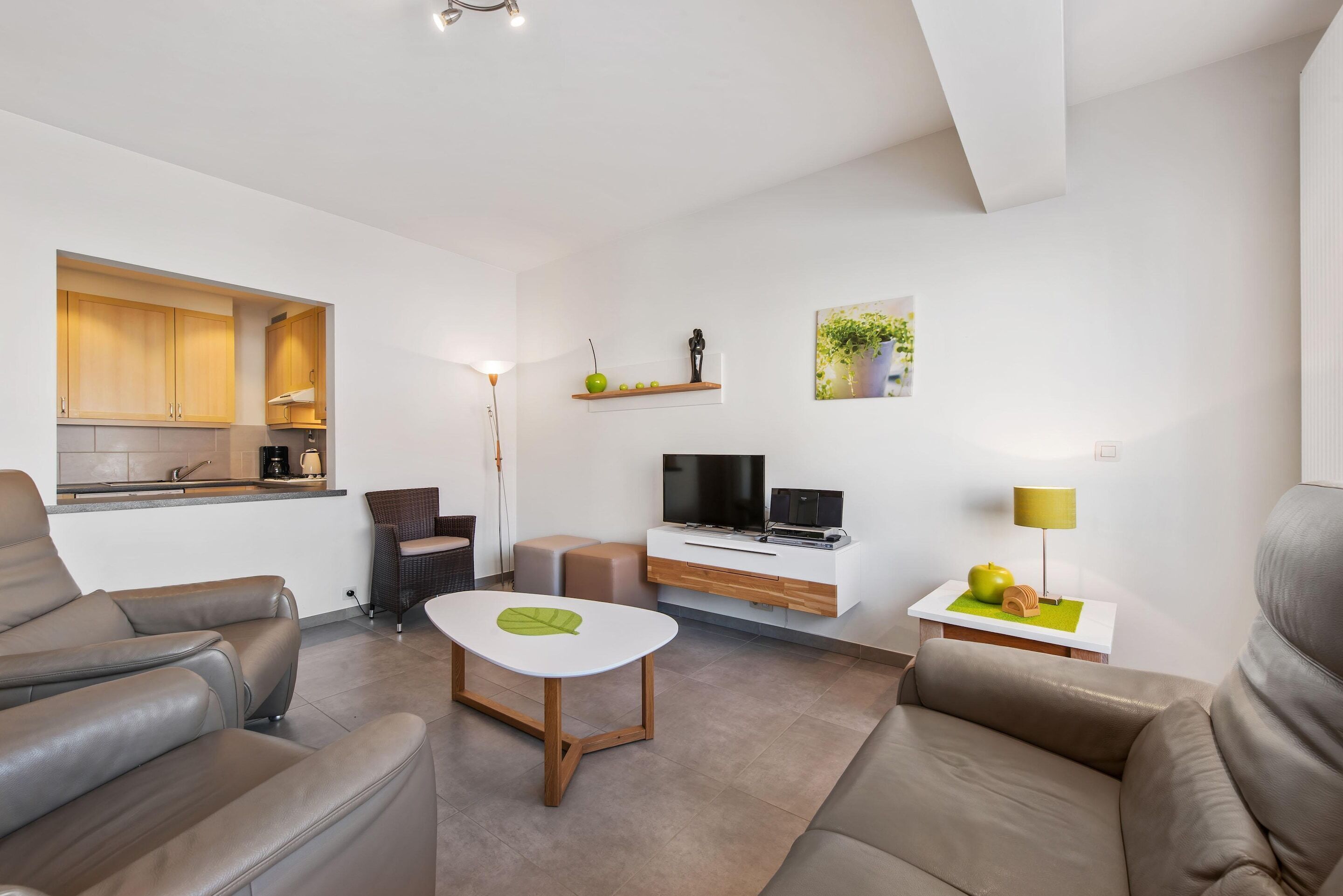 Uma sala de estar moderna com sofá, mesa de centro, TV e área de cozinha com armários e bancada.