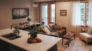 Een moderne keuken met een groot schiereiland, een eethoek met tafel en stoelen, een woonkamer met een bank en een salontafel, en een raam met gordijnen.