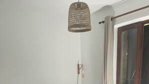 Et værelse med to enkeltsenge, en hængende lampe, et vindue med gardiner og et flisegulv.