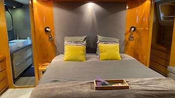 A compact bedroom with a bed, two pillows, a bedside table, and a small wooden tray with flowers.