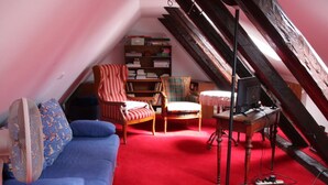 A cozy attic room with a red carpet, a blue sofa, a striped armchair, a plaid armchair, and a bookshelf. - Cozy Apartment on the Canal (Friedrichstadt)