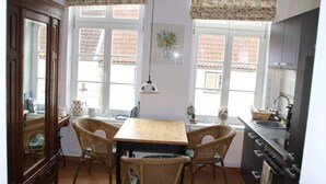 A kitchen with a wooden table and four wicker chairs, large windows with floral blinds, and a dark-colored refrigerator. - Cozy Apartment on the Canal (Friedrichstadt)