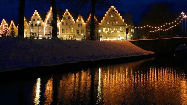 A snow-covered building with a traditional architectural style, illuminated by warm lights, reflecting on a body of water. - Cozy Apartment on the Canal (Friedrichstadt)