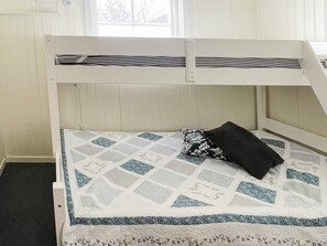 Una cama litera con colchón acolchado, un almohadón estampado con motivos florales y una ventana que da a vistas de árboles.