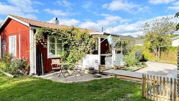 A red house with a white porch, a garden, and a wooden fence.