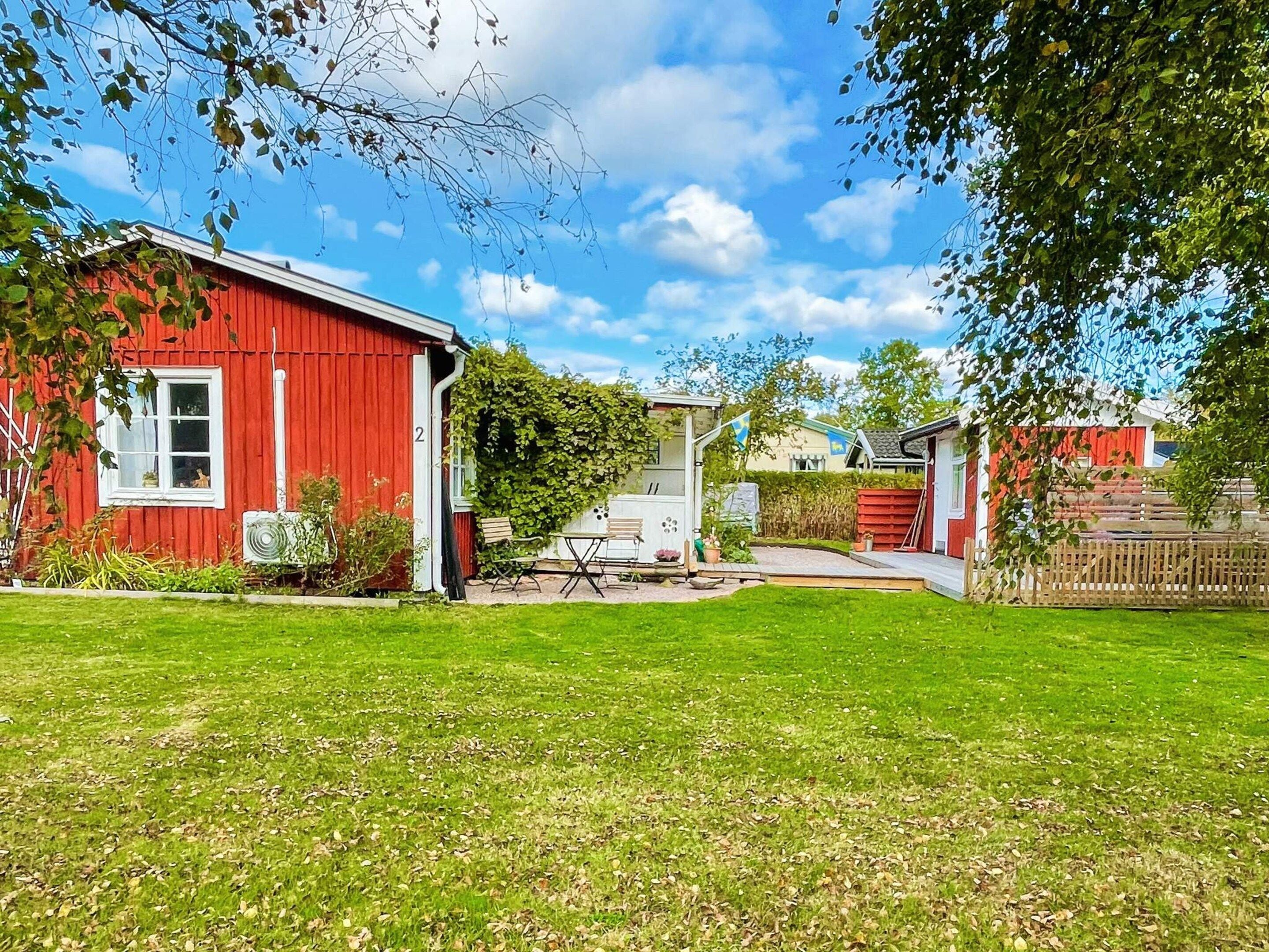 A red building with a white window, a small patio with a table and chairs, and a grassy yard.