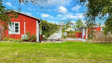 A red building with a white window, a small patio with a table and chairs, and a grassy yard.