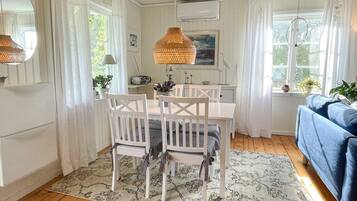 Un comedor con una mesa y sillas blancas, una lámpara colgante y vistas al exterior a través de una ventana.