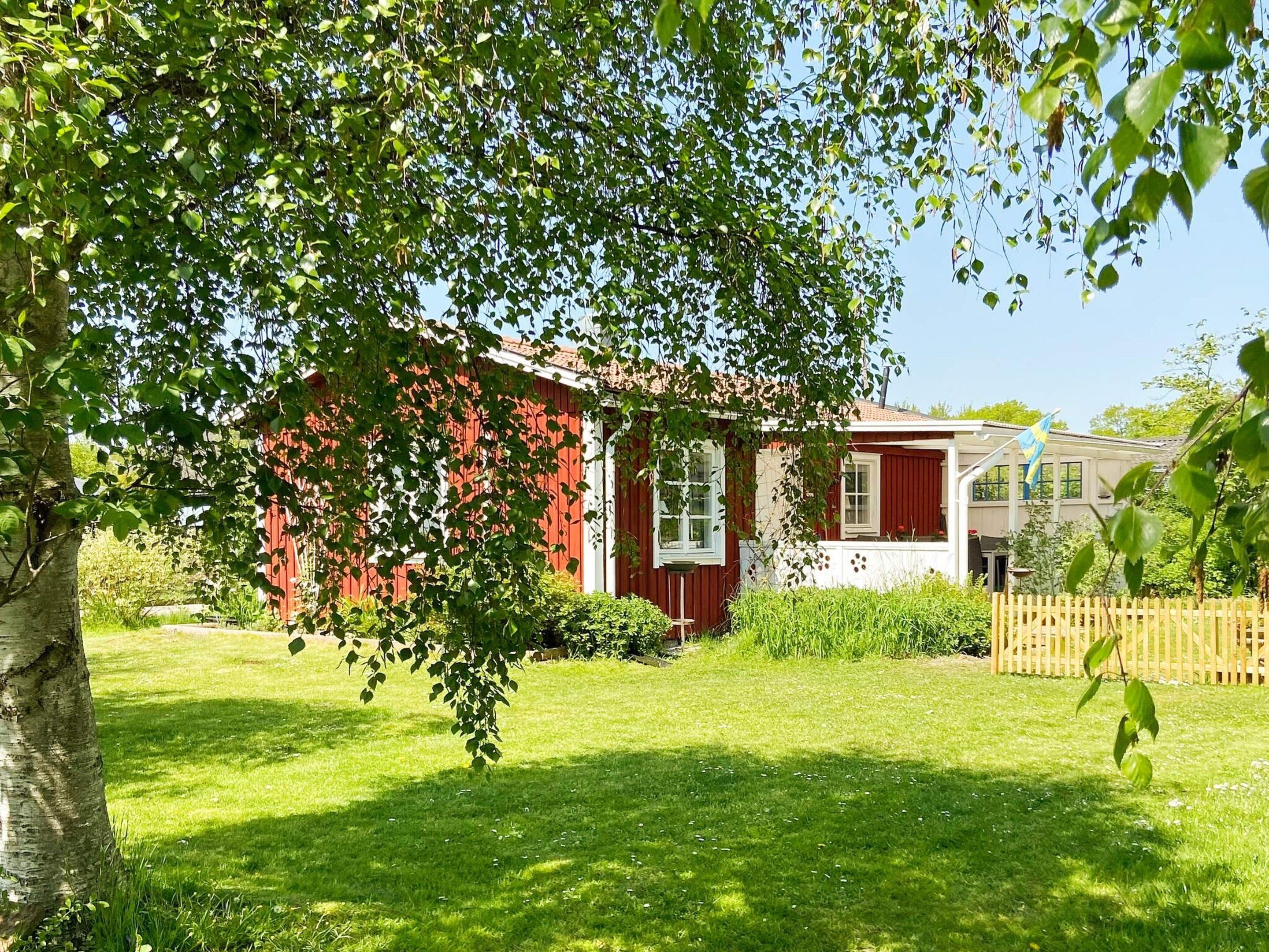 A red building with a white window, surrounded by green grass and trees.