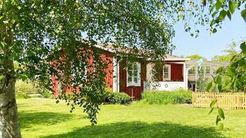 A red building with a white window, surrounded by green grass and trees.