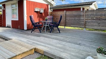 A wooden deck with a red building, outdoor furniture, and a fenced area.