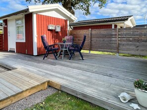 A wooden deck with a red building, outdoor furniture, and a fenced area. - 4 Person Holiday Home in Farjestaden (Farjestaden)
