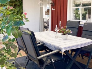 Un coin repas avec une table dressée pour deux personnes, des chaises, une plante en pot et une fenêtre donnant sur un beau paysage.