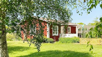 A red building with a white window, surrounded by green grass and trees.