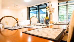 A dining table with placemats, chairs, a bottle of wine, and a vase with flowers. - Welcome to Tropica Bliss! Just 1.6 KM from Darwin CBD (Stuart Park)