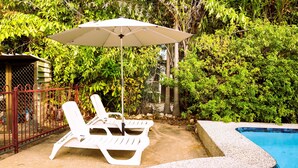 A pool area with white lounge chairs and an umbrella, surrounded by dense greenery. - Welcome to Tropica Bliss! Just 1.6 KM from Darwin CBD (Stuart Park)