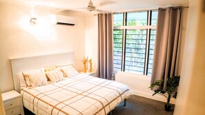 A bedroom with a large bed, a nightstand, a potted plant, and a window with curtains. - Welcome to Tropica Bliss! Just 1.6 KM from Darwin CBD (Stuart Park)