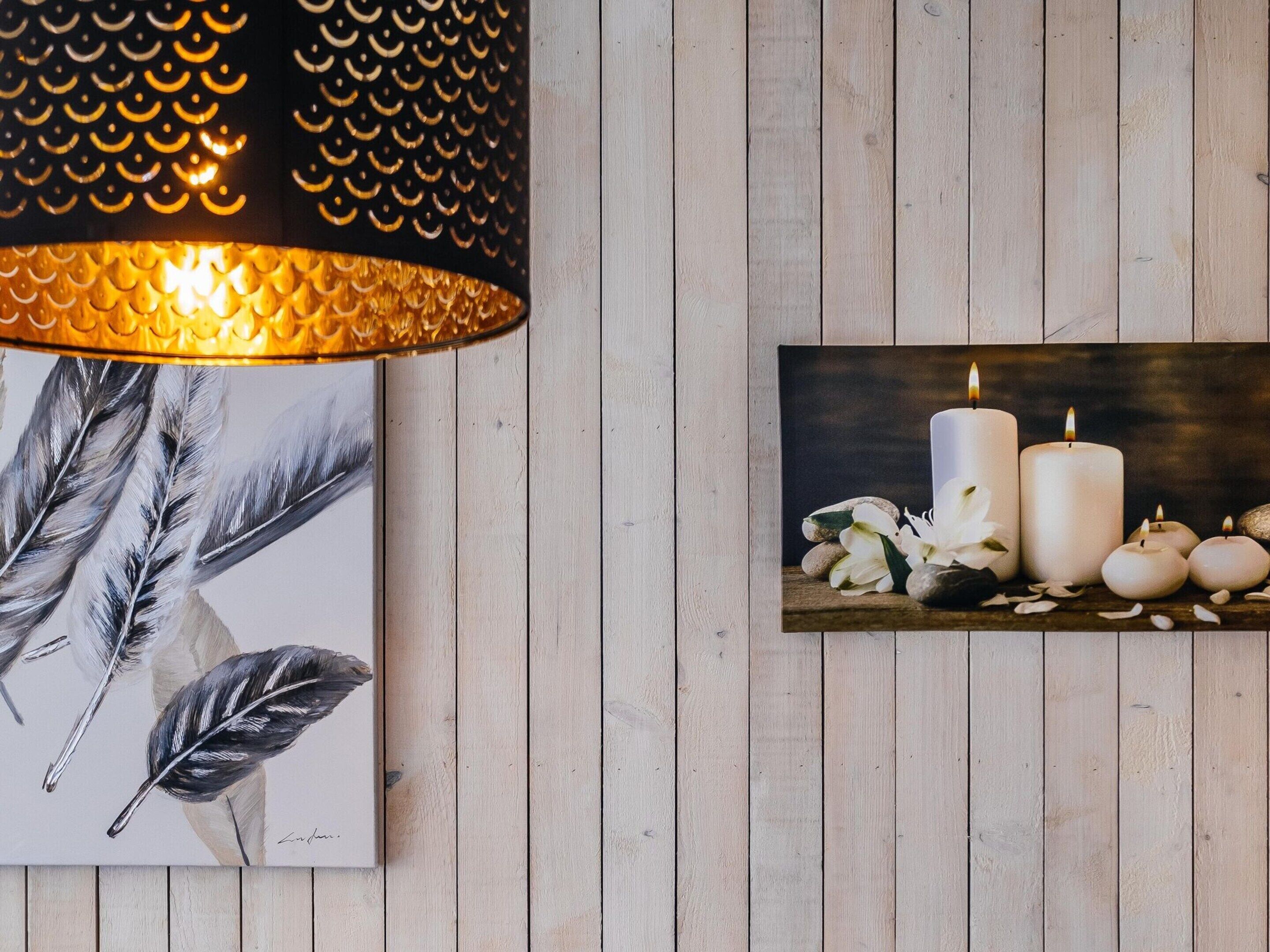 Eine Wand mit Holzpaneelen, eine schwarze Lampenleiste und ein gerahmtes Kunstwerk mit weißen Kerzen und Blumen.