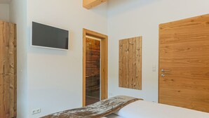 Une chambre à coucher avec un lit, une armoire en bois, un téléviseur fixé au mur et une porte en bois.