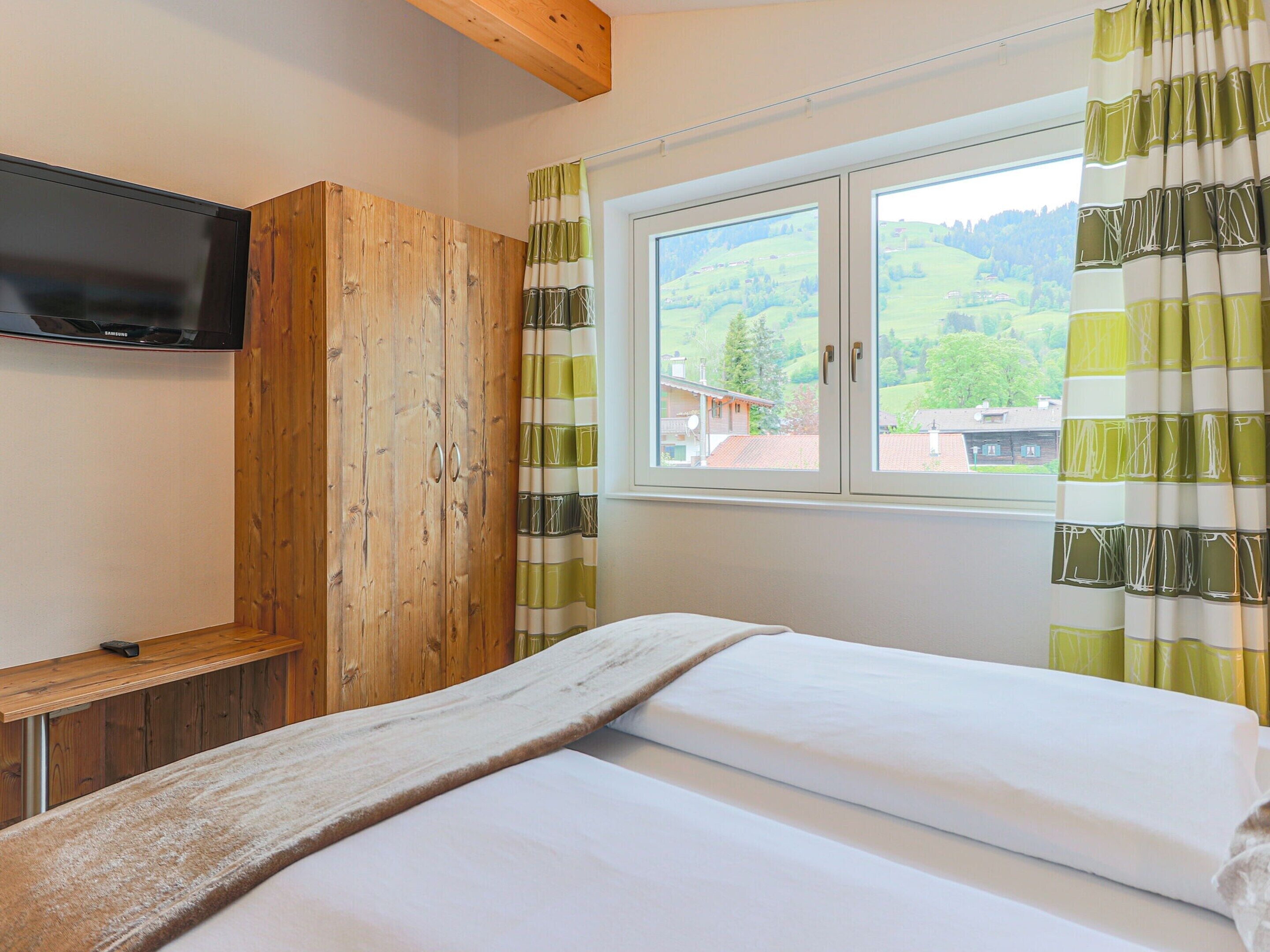 A bedroom with a bed, wooden wardrobe, and a TV on the wall.