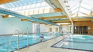 An indoor swimming pool with clear water, tiled floors, and a wooden ceiling structure. - Hliday Home on a Holiday Park in Ebeltoft (Ebeltoft)