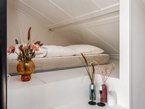 Ein Schlafzimmer mit einem Bett, weißer Bettwäsche und einer Vase mit Blumen auf dem Boden.
