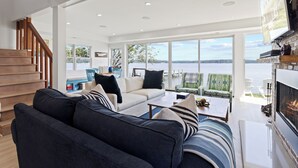 A spacious living room with a large sofa, a fireplace, and a view of a lake.
