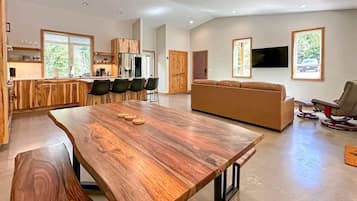 A spacious living area with a large wooden table, a sofa, and a television mounted on the wall.