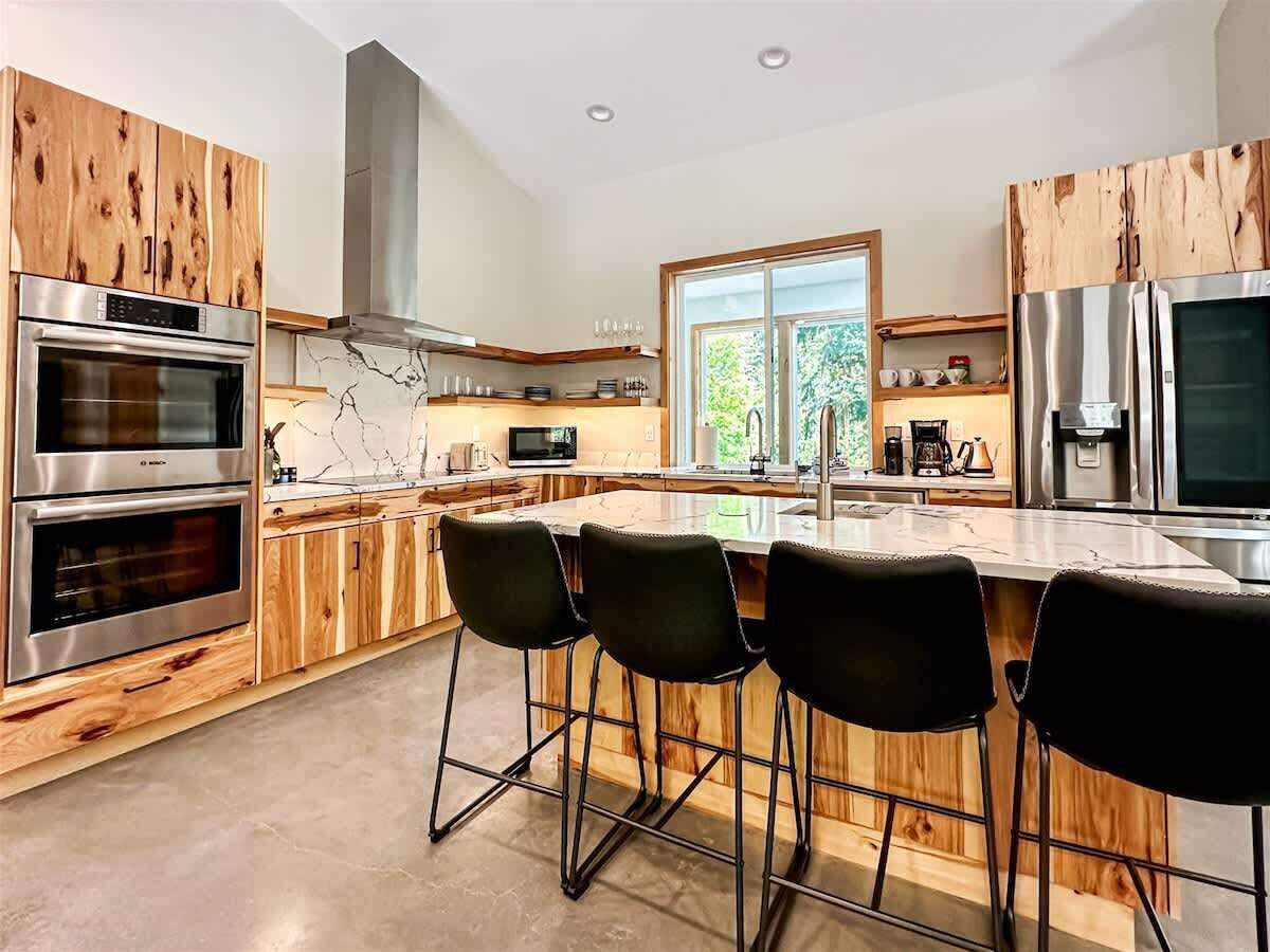 Una cocina moderna con armarios de madera, electrodomésticos de acero inoxidable y una isla central con taburetes de bar.