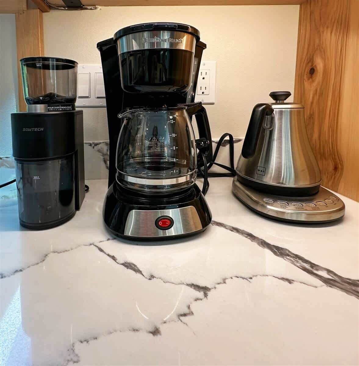 A coffee maker, a scale, and a kettle on a marble countertop.