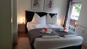 Un lit bien fait, avec du linge de lit blanc et deux serviettes attachées par des rubans rouges, une lampe de chevet et une fenêtre avec des rideaux.