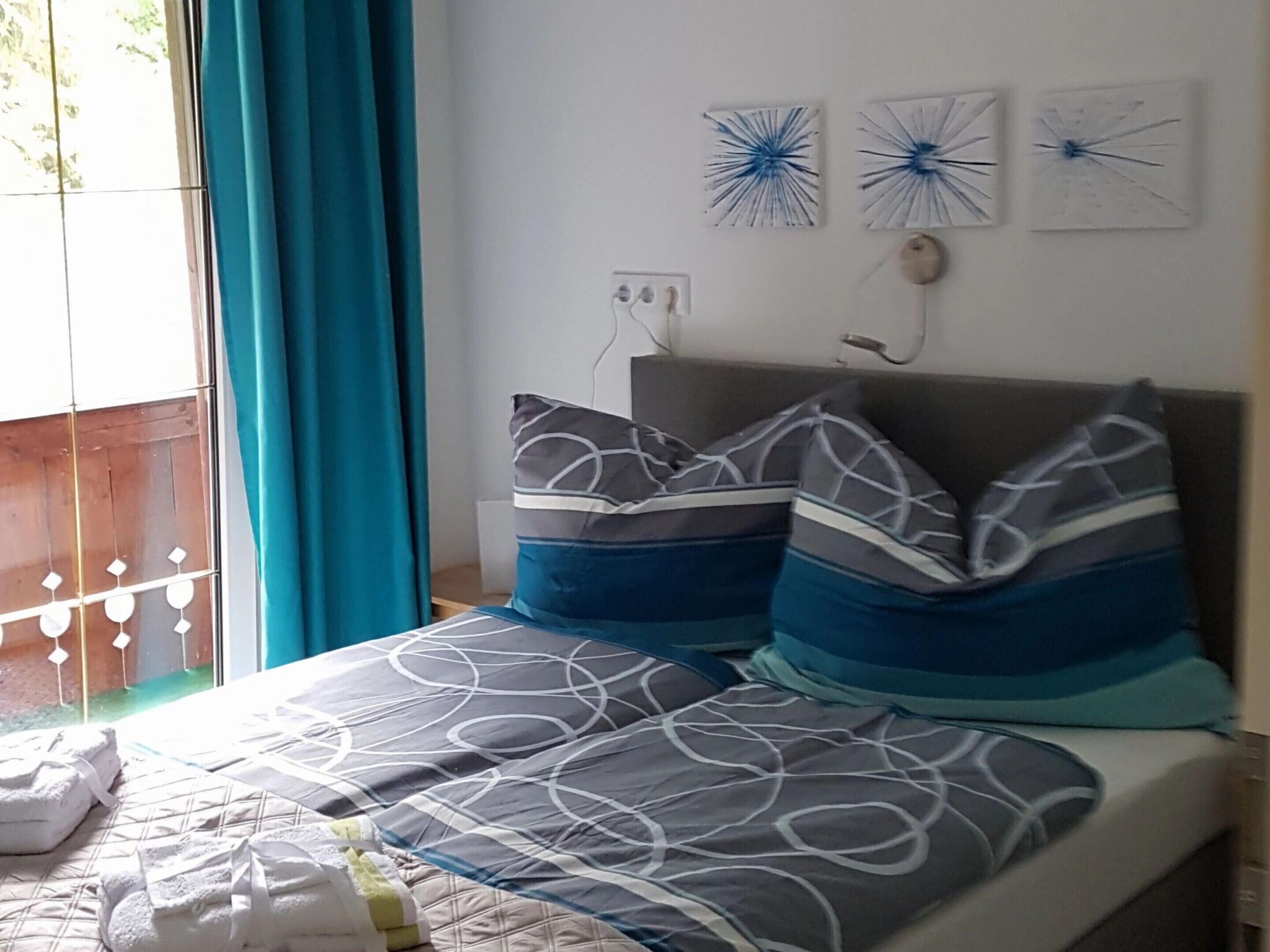 Una camera da letto con un letto, cuscini, una finestra con tende e decorazioni murali.