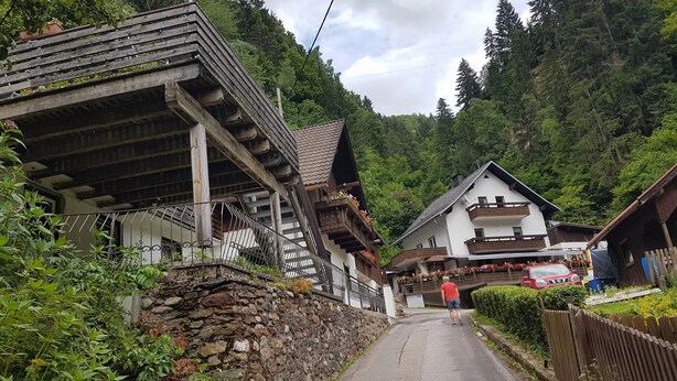 Une rue étroite bordée de maisons traditionnelles en bois, de murs en pierre, et où l’on aperçoit une personne qui marche.