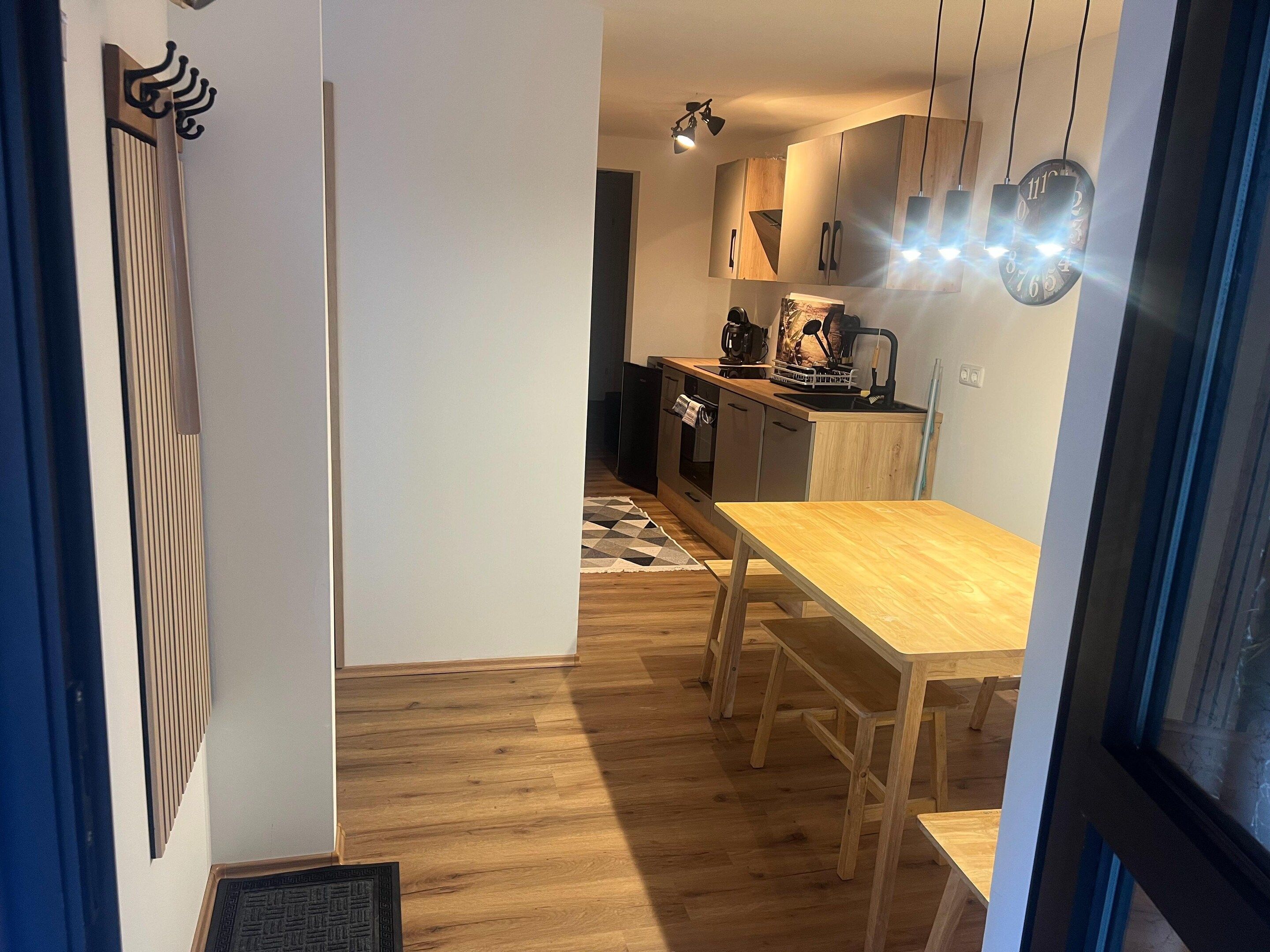 A modern kitchen with wooden cabinets, a dining table, and a patterned rug.